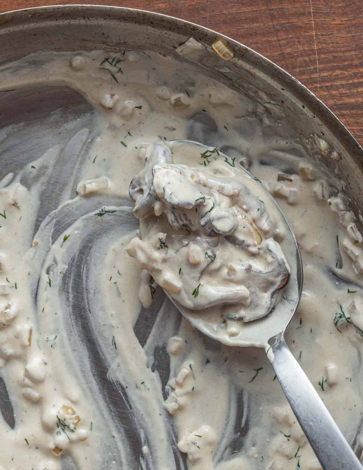 A spoonful of creamy mushroom sauce with fresh dill in a pan. 
