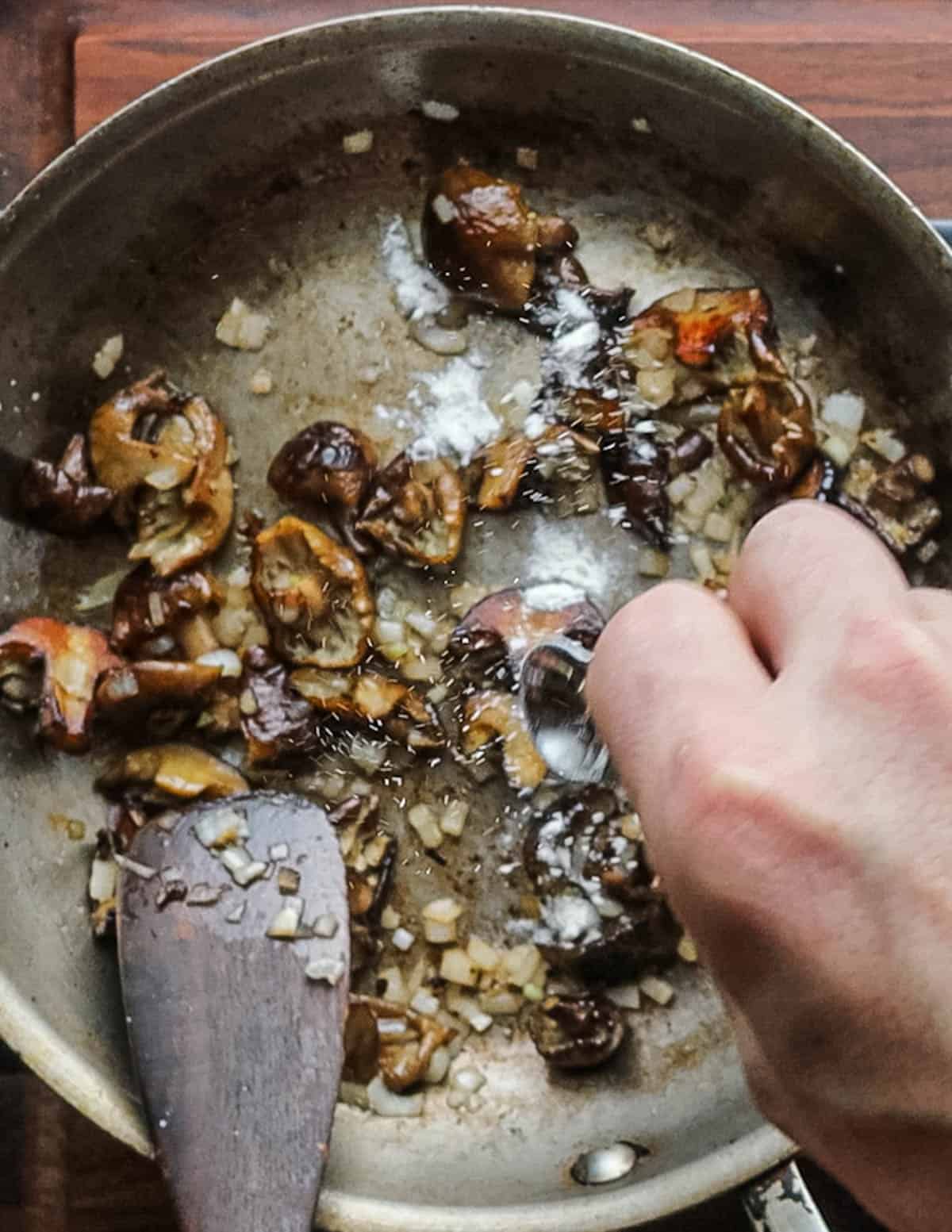 Sprinkling in flour to a pan of cooked mushrooms. 