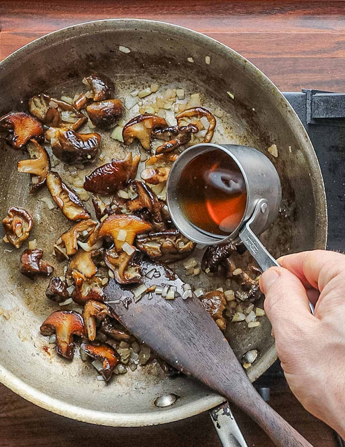 Pouring brandy into a pan of cooking mushrooms. 