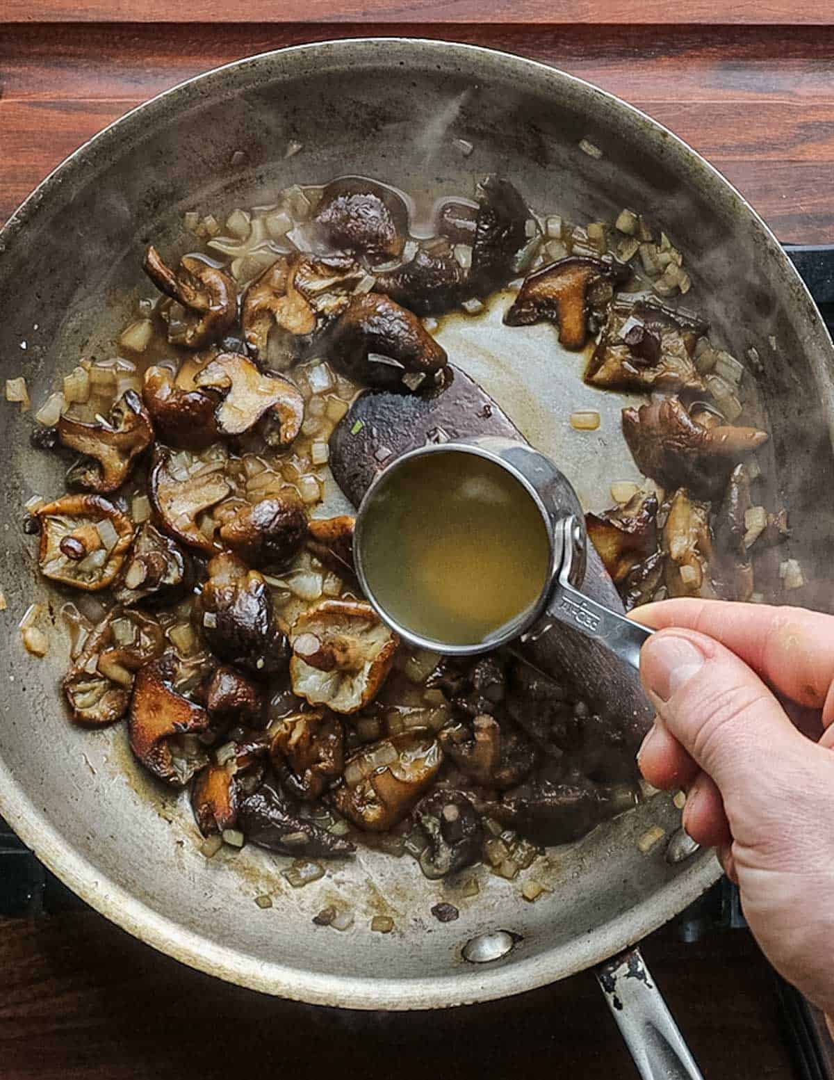 Adding chicken stock to a pan of honey mushrooms. 