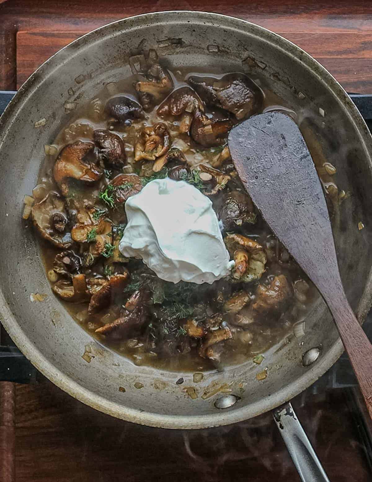 Adding sour cream to a pan of honey mushrooms. 