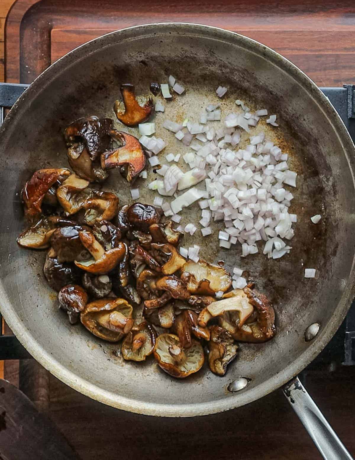 Well cooked, browned honey mushrooms cooking in a pan with shallots. 