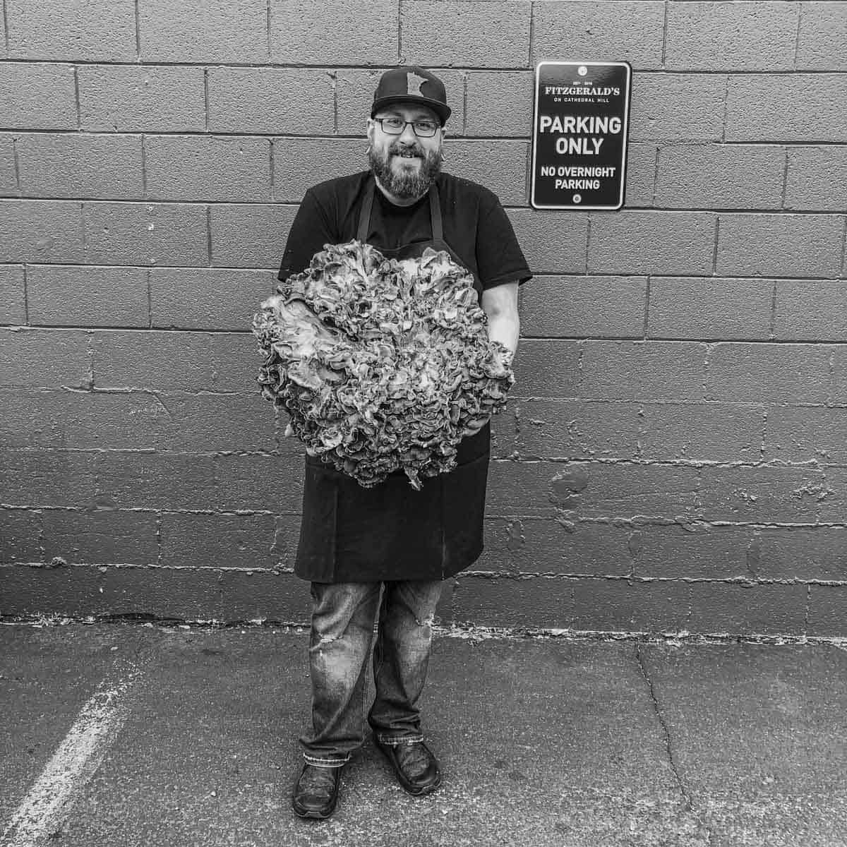 A chef standing in front of a brick building holding a 30 pound hen of the woods. 