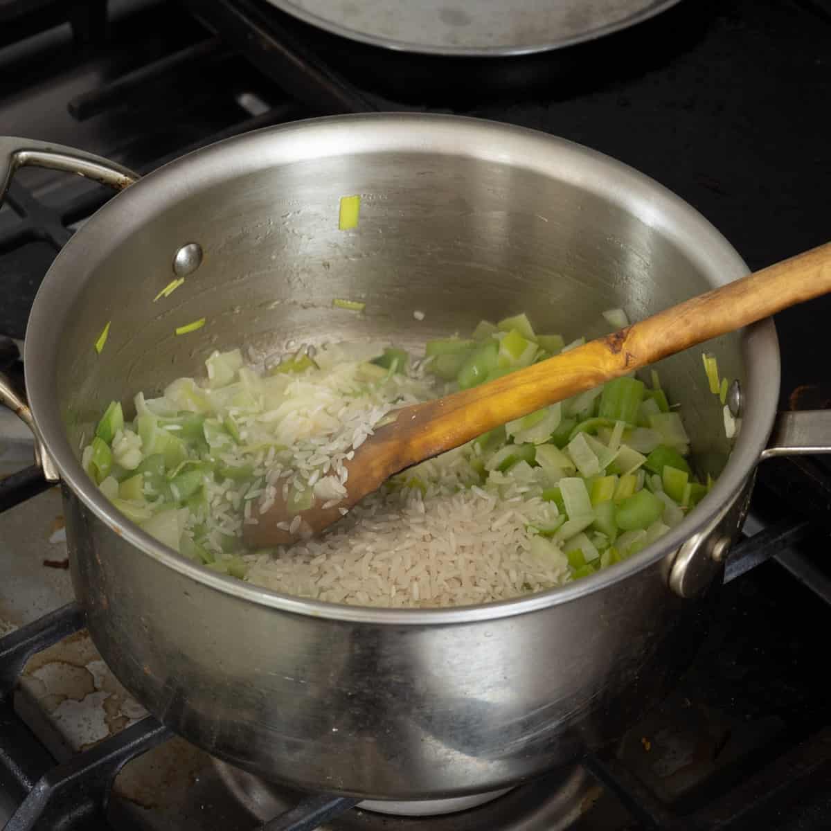 adding rice to a pot of celery, onion and leek