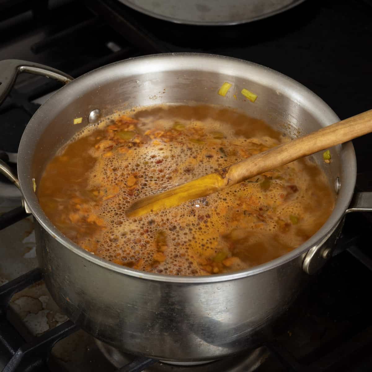 adding stock to a pot of soup