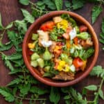 Panzanella con verdolagas in a wooden bowl surrounded by tomato leaves