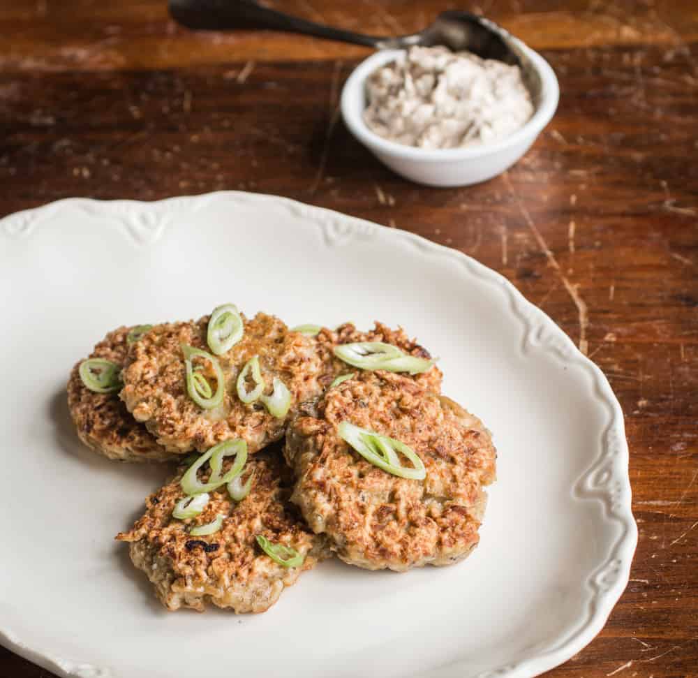 Mushroom fritters on a plate with green onions, next to a bowl of onion sour cream. 