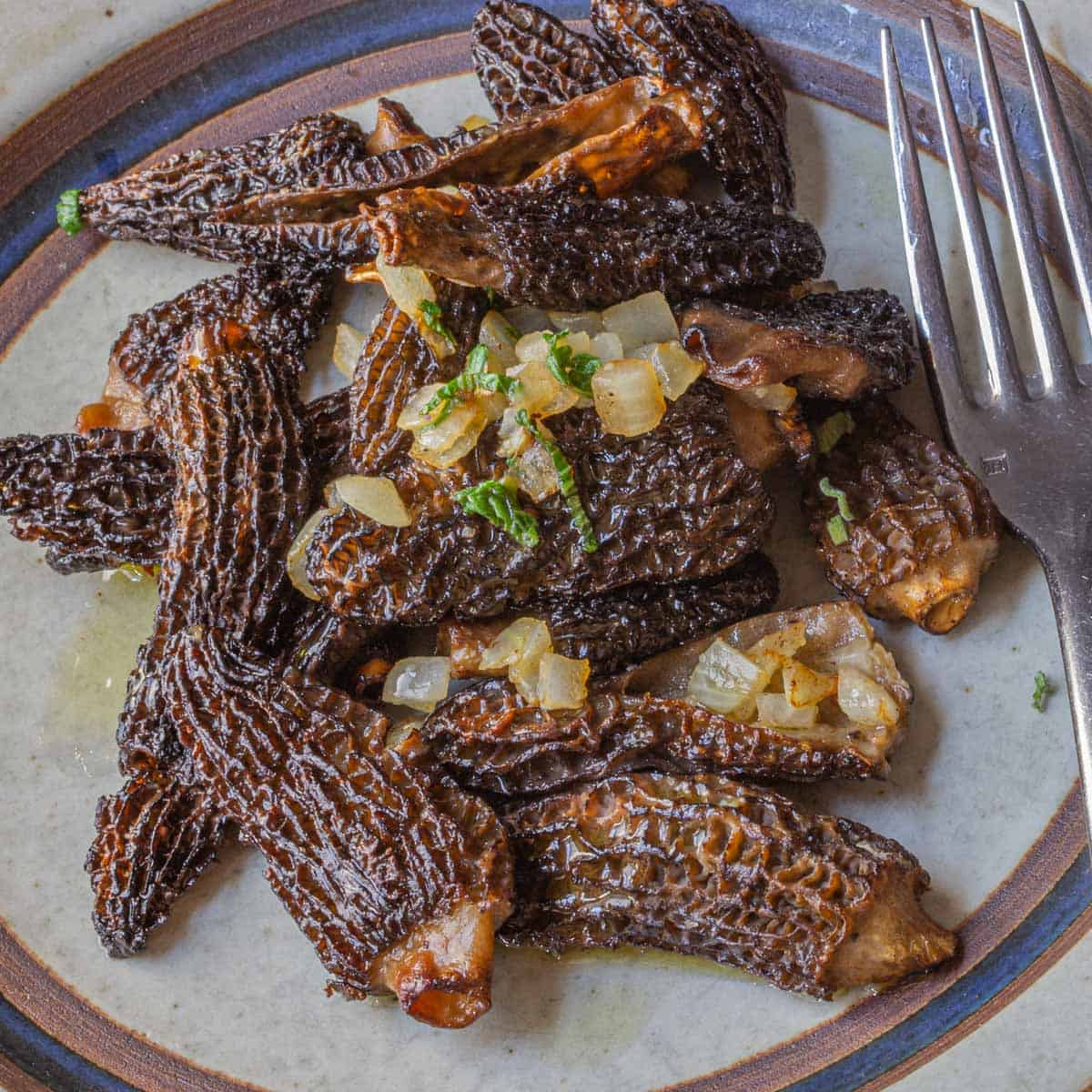 Cooked morel mushroms on a plate with a fork. 