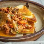 A bowl of cooked mushrooms and sausage with toast.