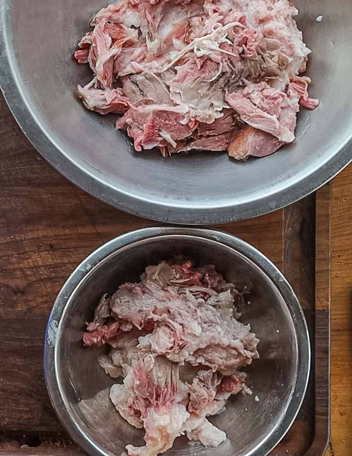 Two bowls of cooked meat and fat from picking a cooked pork head. 