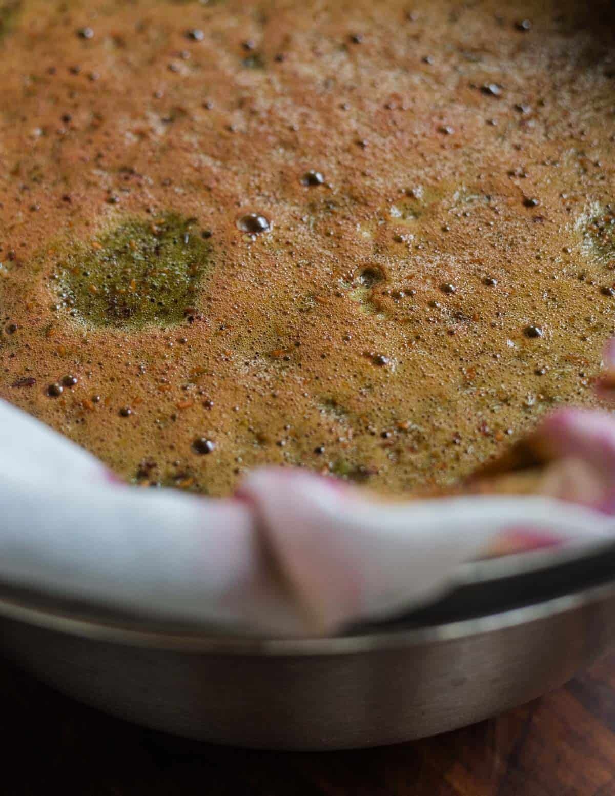A close up image of the green-ish impurities and foam settling on top of a colander of elderberries.
