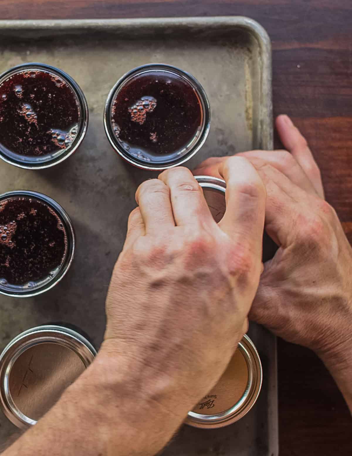 Screwing lids onto jars of elderberry jelly.