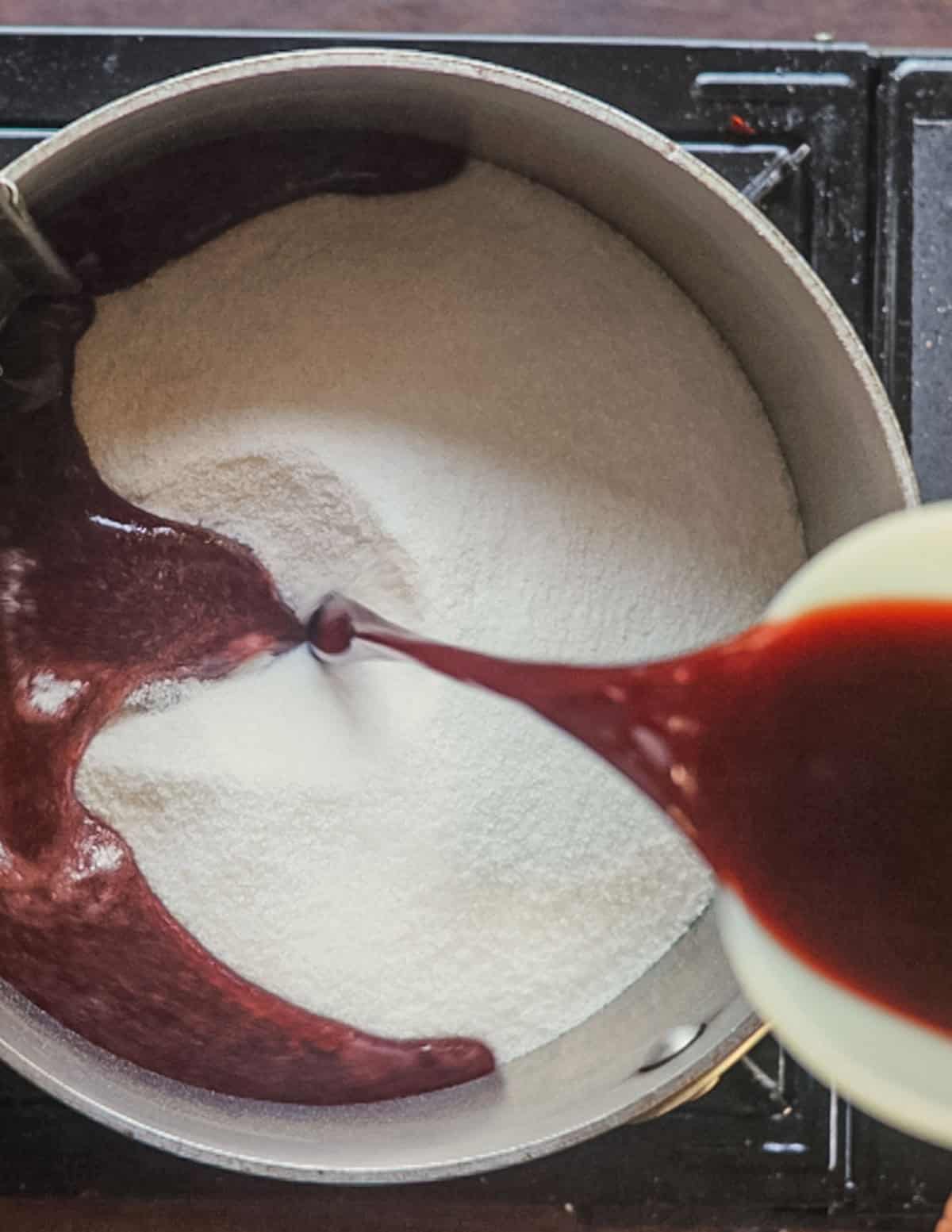 Adding elderberry juice to sugar and pectin in a pot.