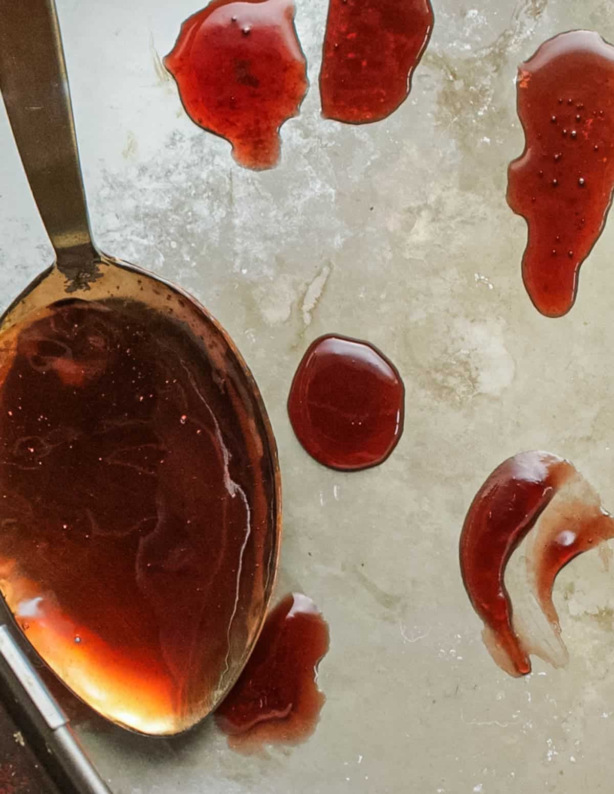 A spoon dropping teaspoons of elderberry jelly onto a frozen plate to test the set of the jelly.