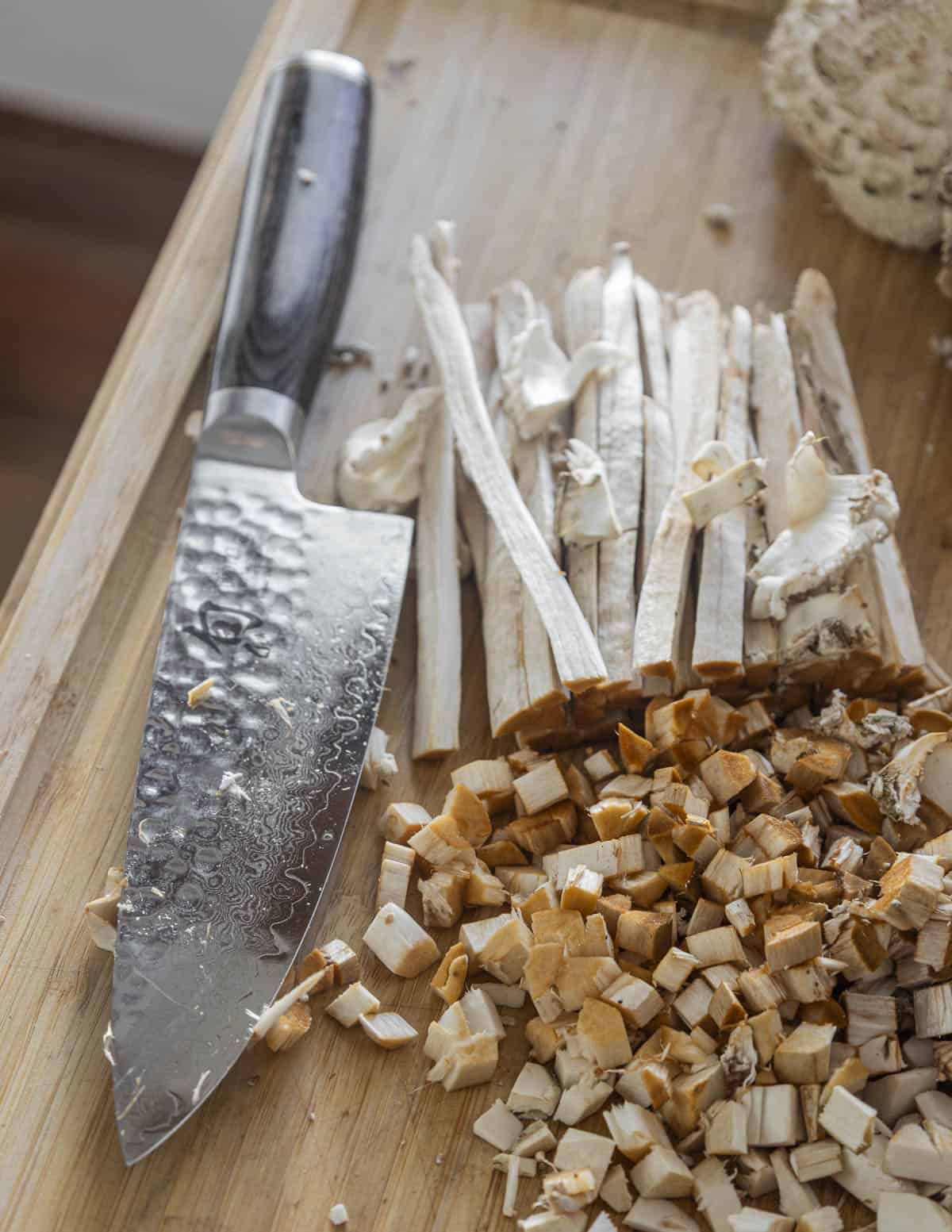 A large amount of shaggy parasol mushroom stems being cut with a chef knife showing orange staining turning to red on the cut stems. 