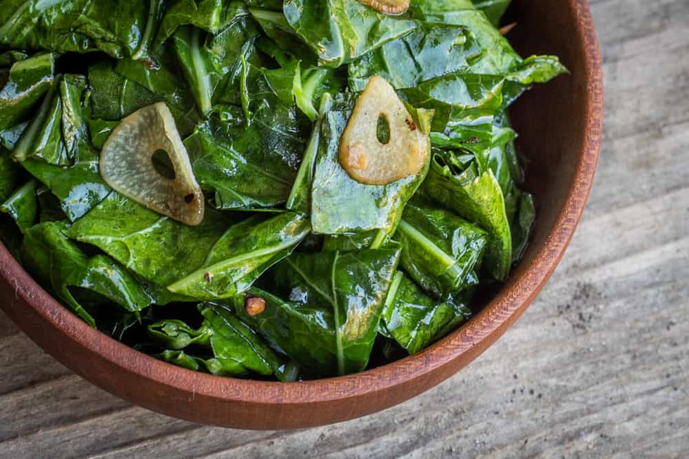 cooked edible broccoli leaves in a wooden bowl on wood background lemon wedge