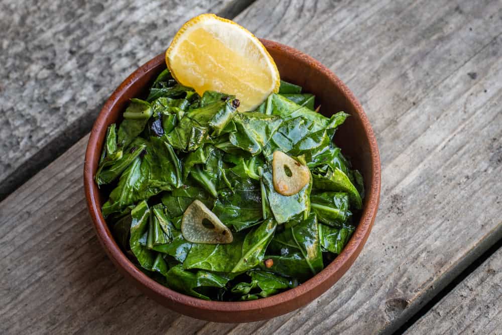 cooked edible broccoli leaves in a wooden bowl on wood background lemon wedge 