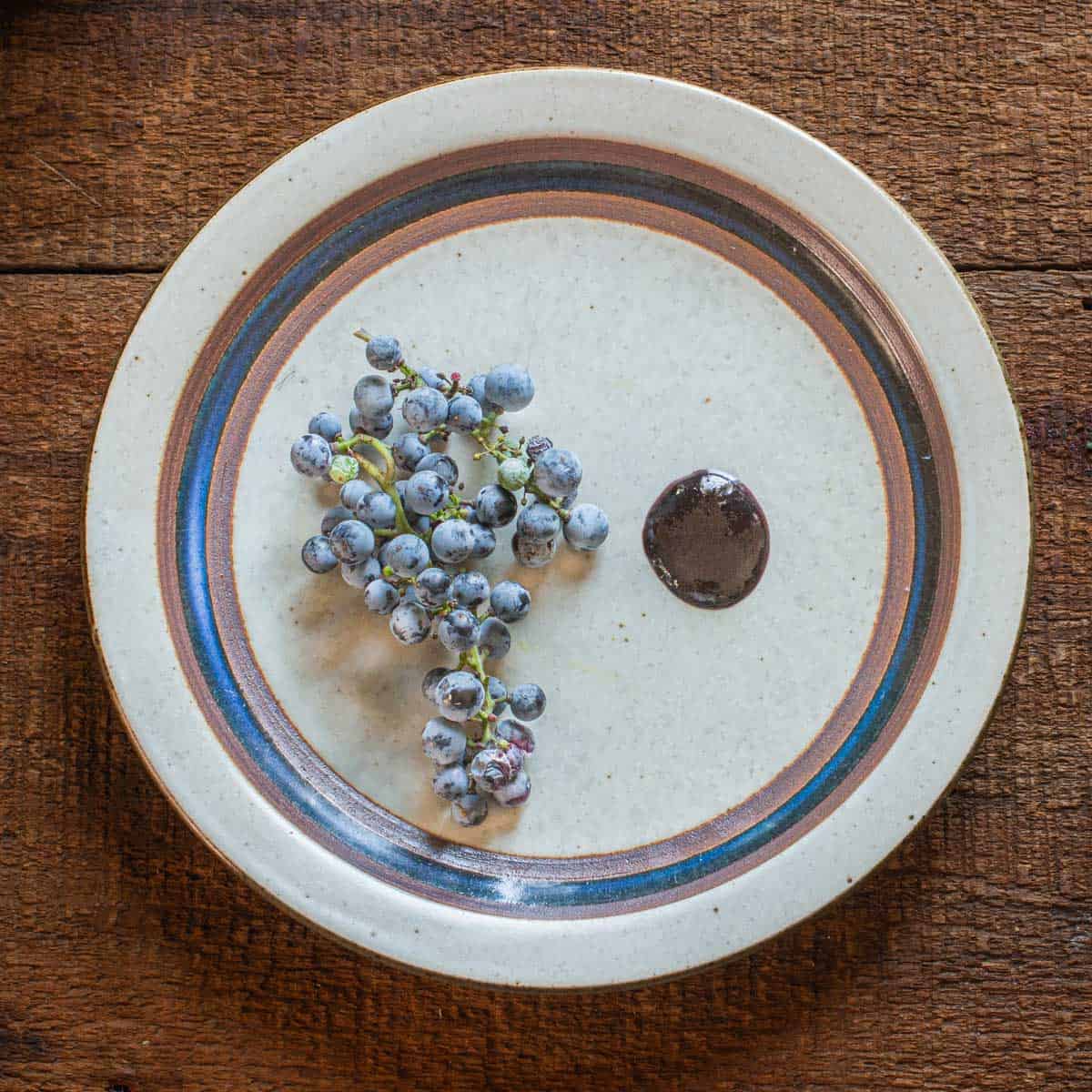 Wild grape molasses or petimezi on a plate next to a cluster of grapes. 