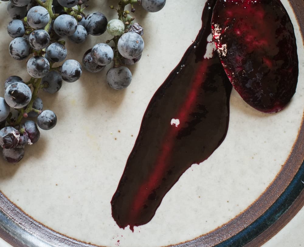 A spoon smearing grape molasses or Greek petimezi on a plate. 