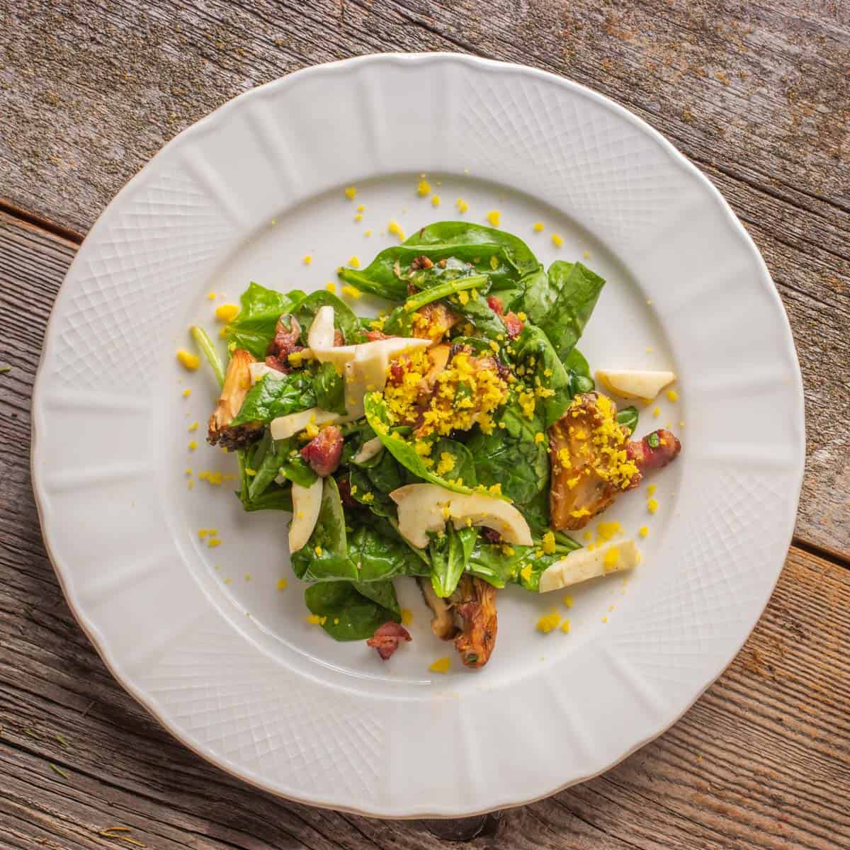 Spinach mushroom salad with bacon and grated egg yolk on a plate