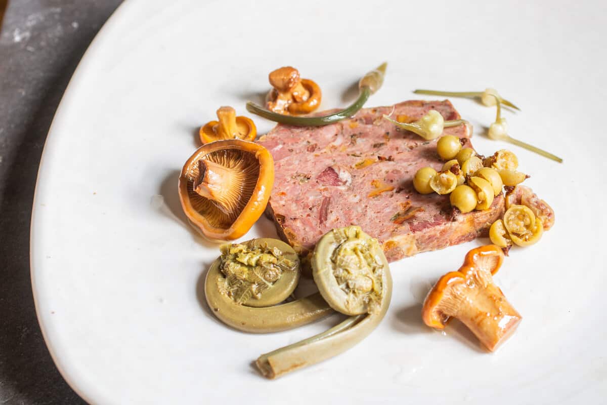 a slice of terrine on a plate surrounded by pickled vegetables 