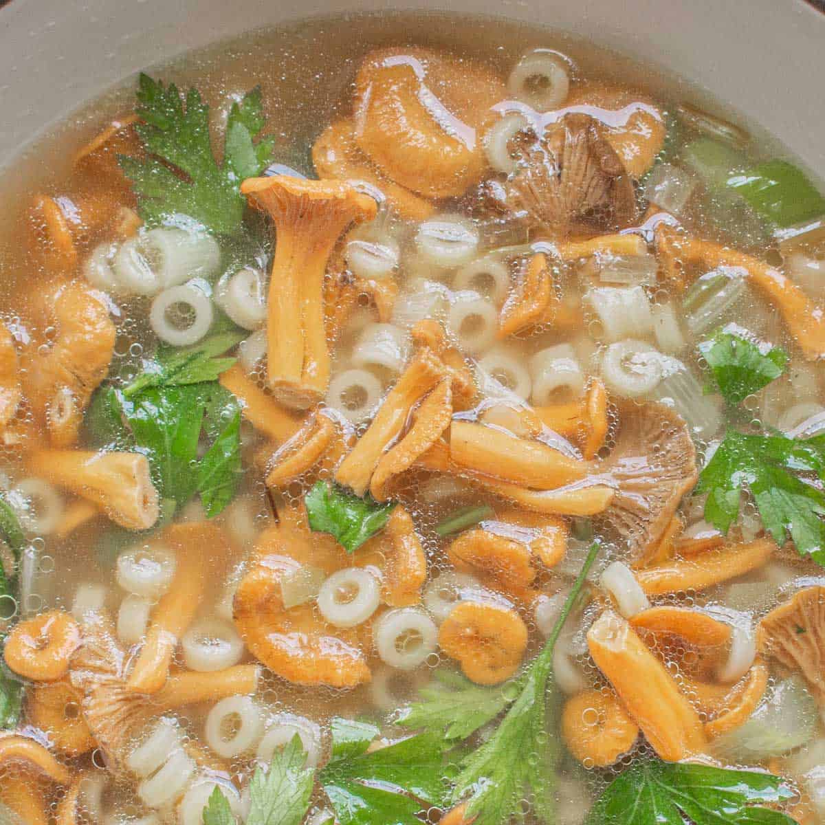 yellow mushrooms in a bowl of broth with herbs and pasta rings 