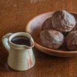 Cooked rounds of blood bread in a bowl next to a pitcher of fresh lamb's blood.