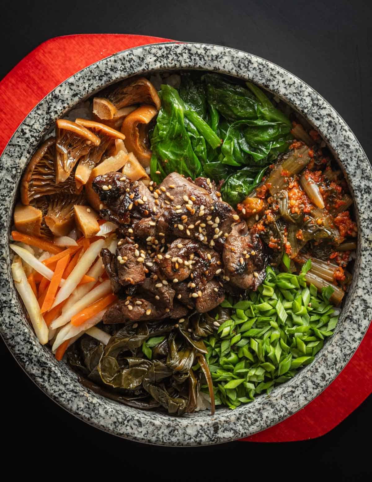 A dish of bibmbap in a granite bowl served with many garnishes including doraji made from bellflower roots.