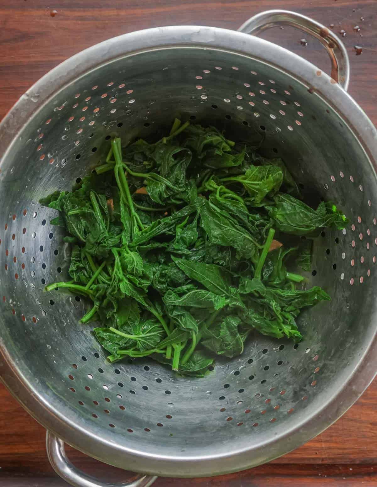 Draining cooked creeping bellflower leaves in a colander.