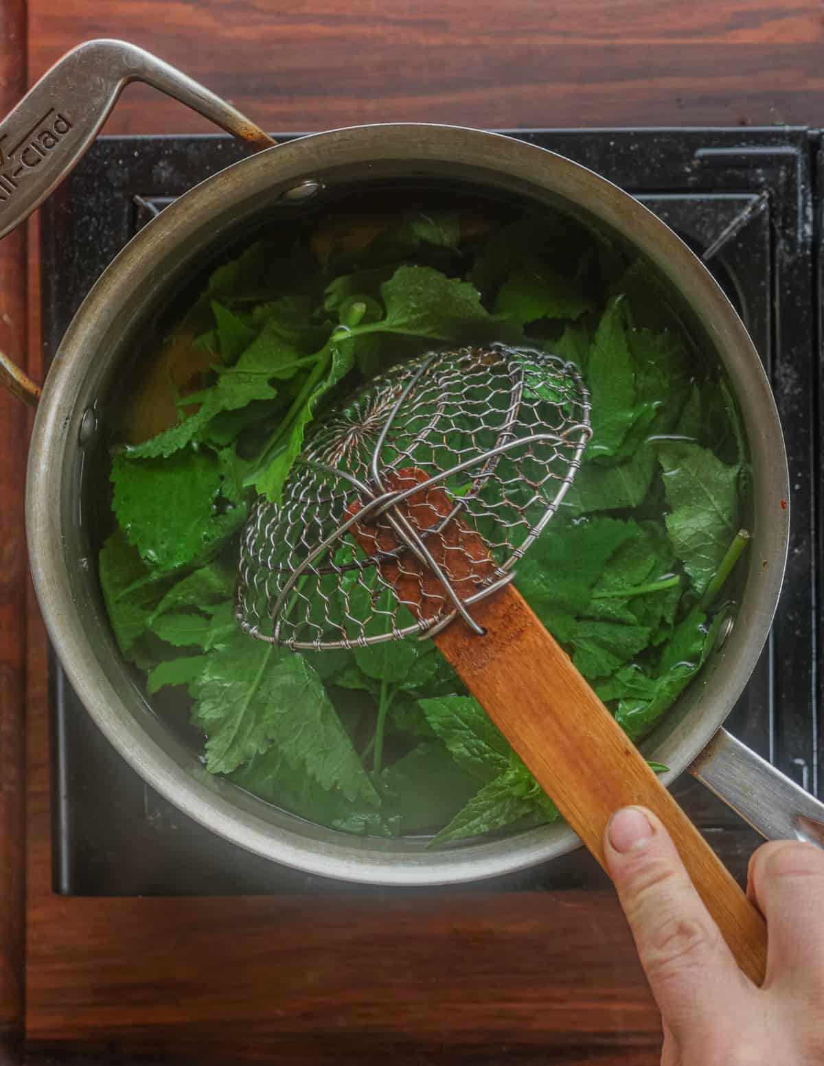 Boiling creeping bellflower greens in a pot of salted water and removing them with a Chinese spyder tool.
