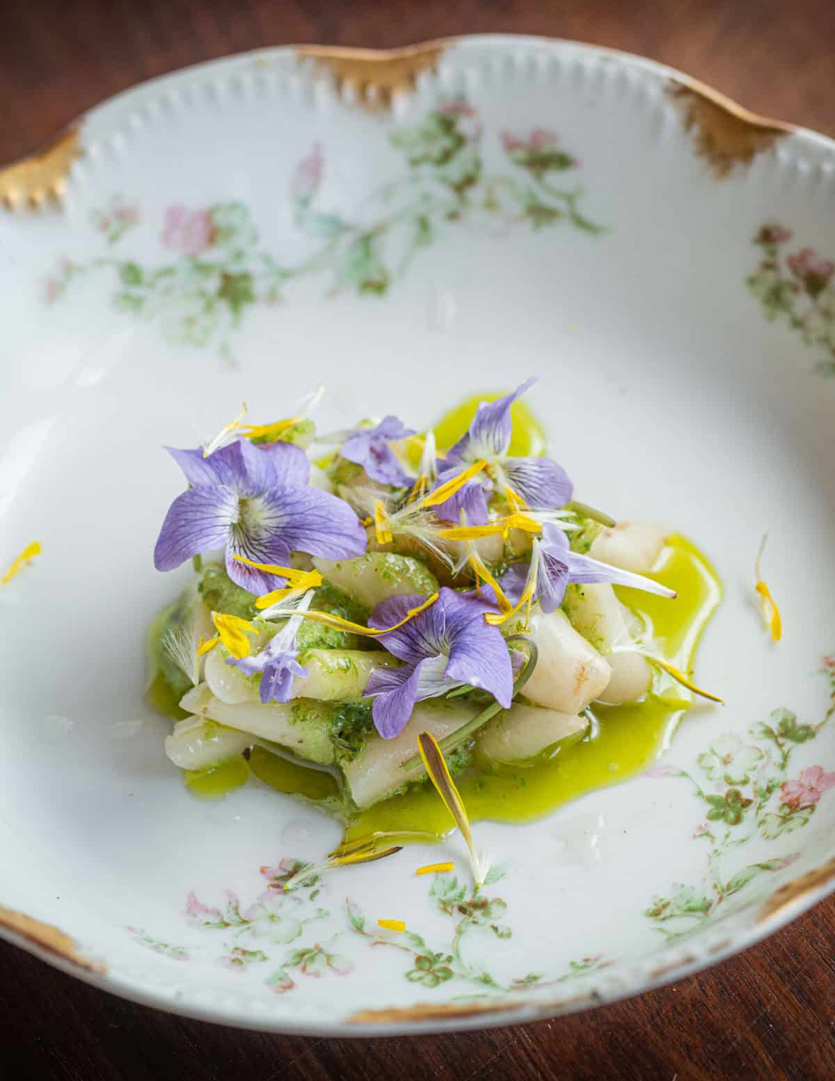 A plate of cooked creeping bellflower roots with ramp butter and wild violet flowers.
