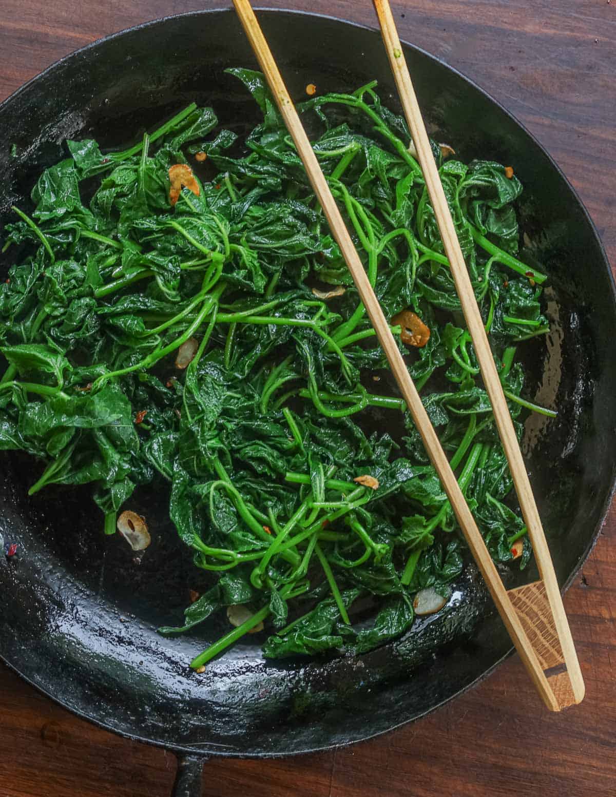 A pan of cooked bellflower leaves being cooked with garlic and chili.