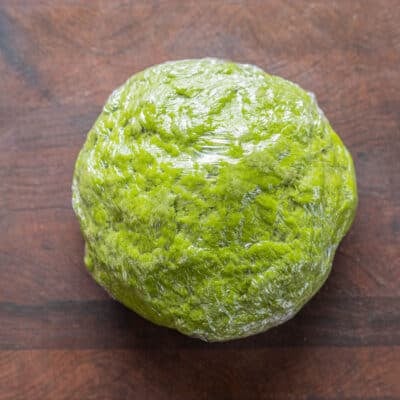 A ball of green pasta dough wrapped in cling film.