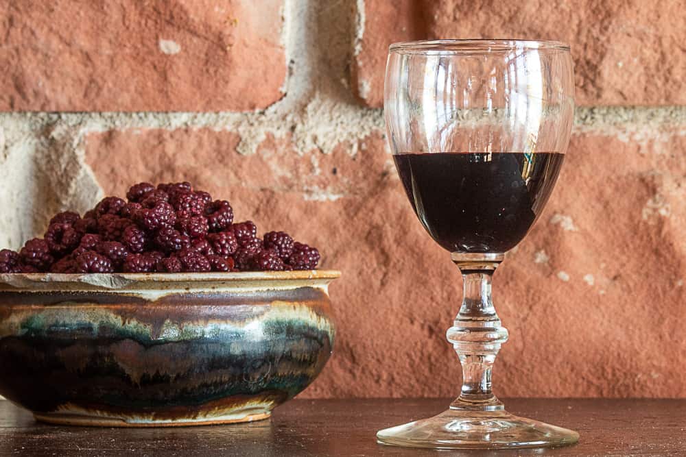 A small glass of cassis liqueur next to a bowl of fruit used to make it. 