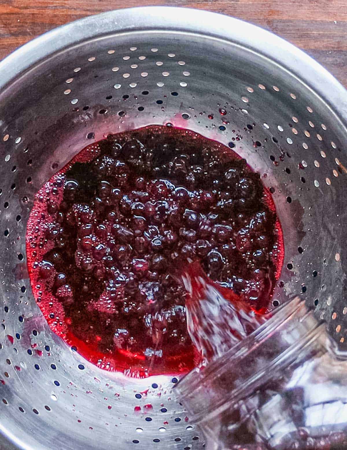 Pouring currants and brandy into a strainer from a jar. 