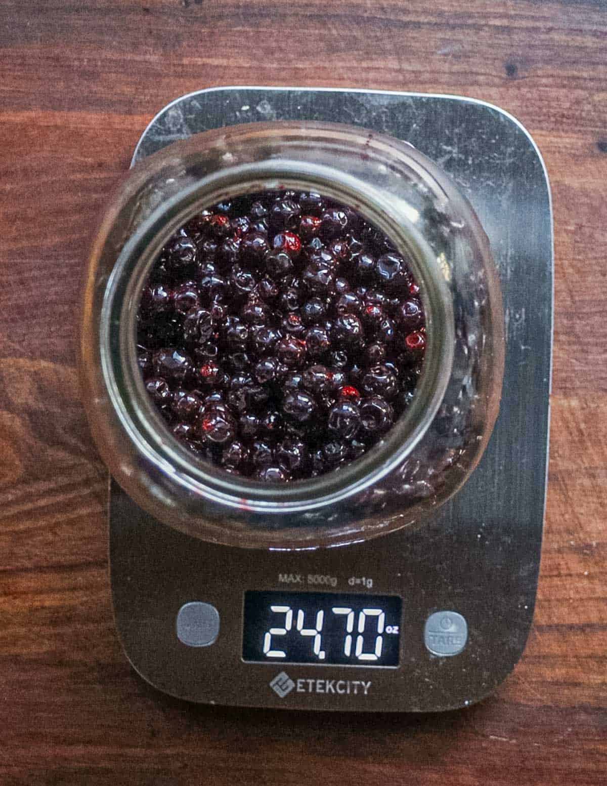 Black currants in a mason jar sitting on a digital scale. 