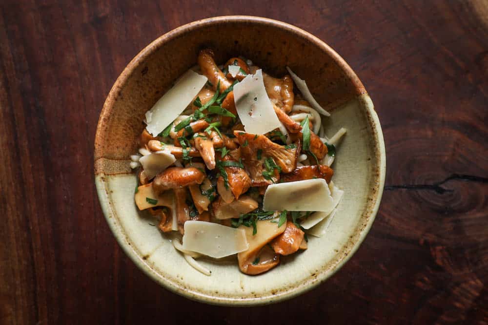 Chanterelle mushroom spaghetti with roasted garlic sauce and herbs in a ceramic bowl on black walnut background 