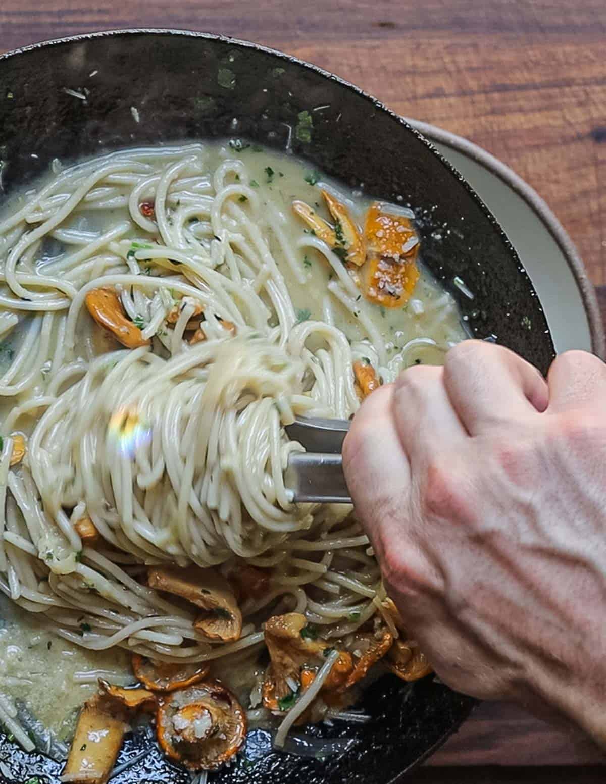 Twirling noodles with a tongs to plate a bowl of mushroom pasta. 
