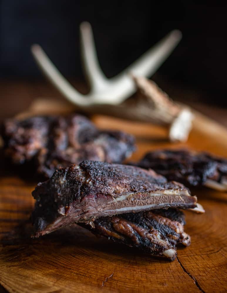 cooked venison ribs on a board with antlers in the background