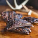 cooked venison or deer ribs with antlers on a board with antlers behind them.