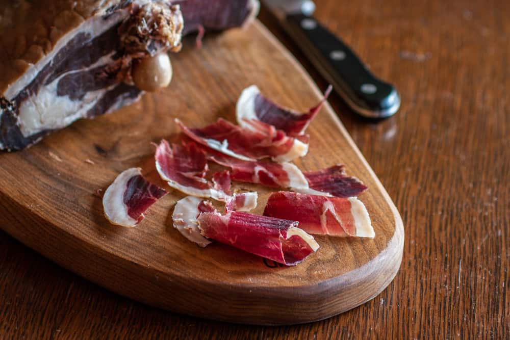 slicing homemade lamb prosciutto on a wooden cutting board 