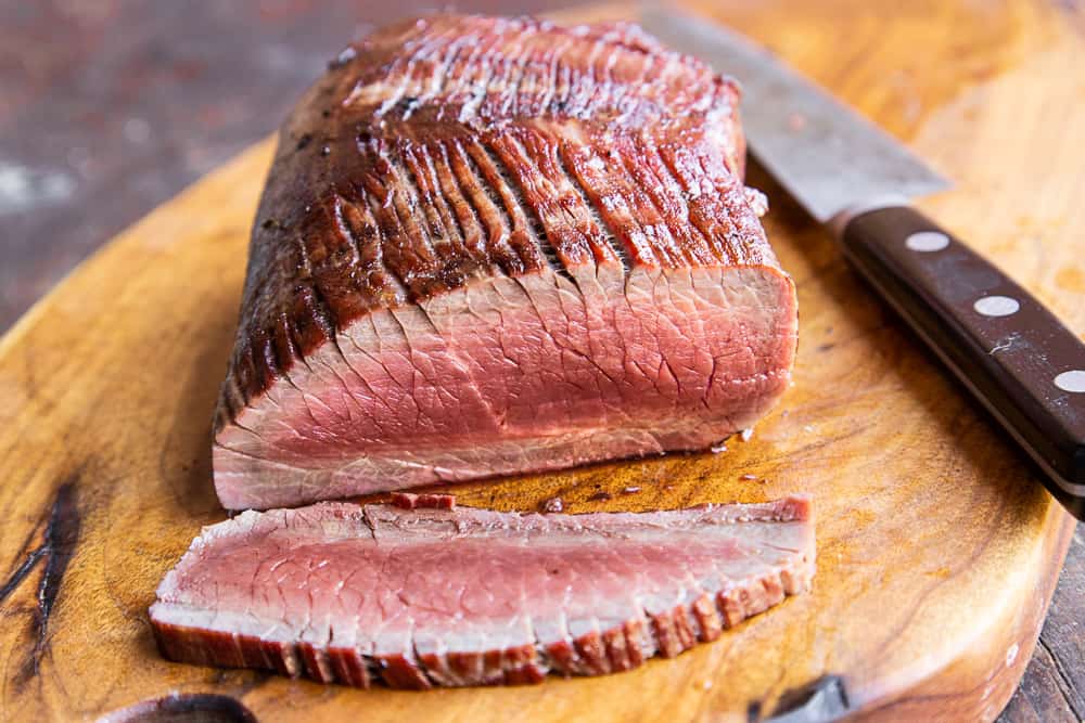 slicing a smoked venison leg roast on a wood cutting board