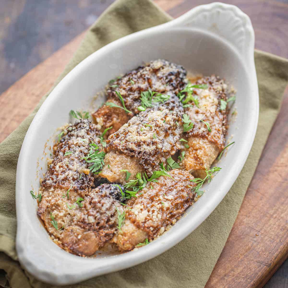 A welsh rarebit dish filled with baked stuffed morels topped with breadcrumbs and herbs on a napkin. 