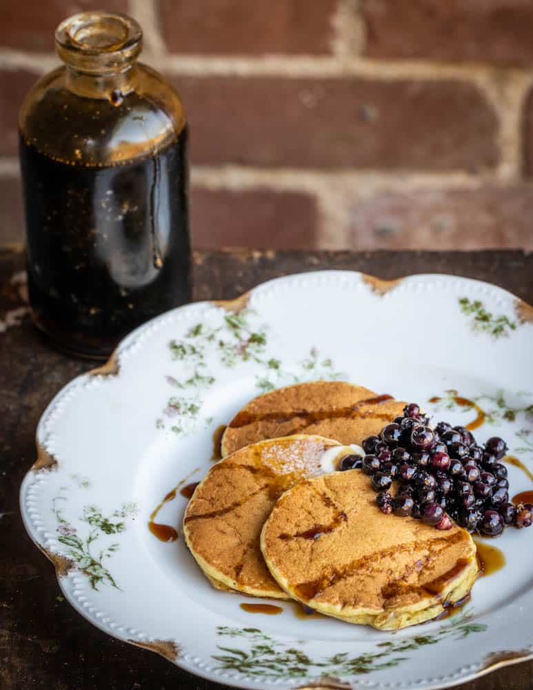 Cattail pollen pancakes with mugolio pine cone syrup and wild blueberries on a plate. 