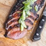 Blackened venison flank steak sliced on a board.