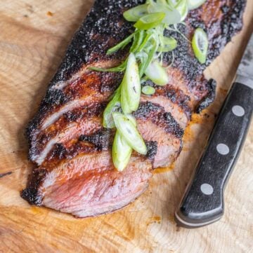 Blackened venison flank steak sliced on a board.