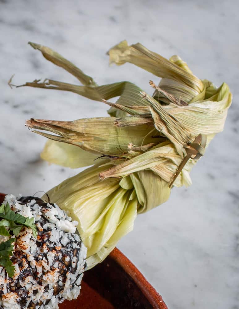Tied husk of corn on an elote with huitlacoche puree