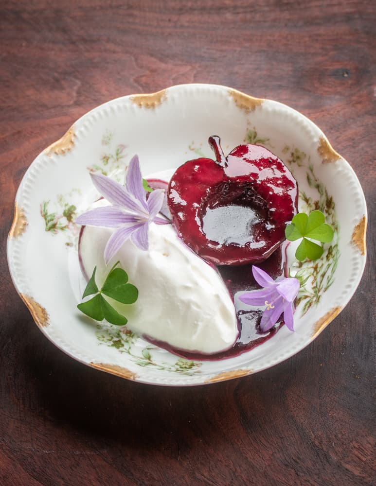 Apples poached in wild grape juice with maple sugar creme fraiche bell flower and wood sorrel 