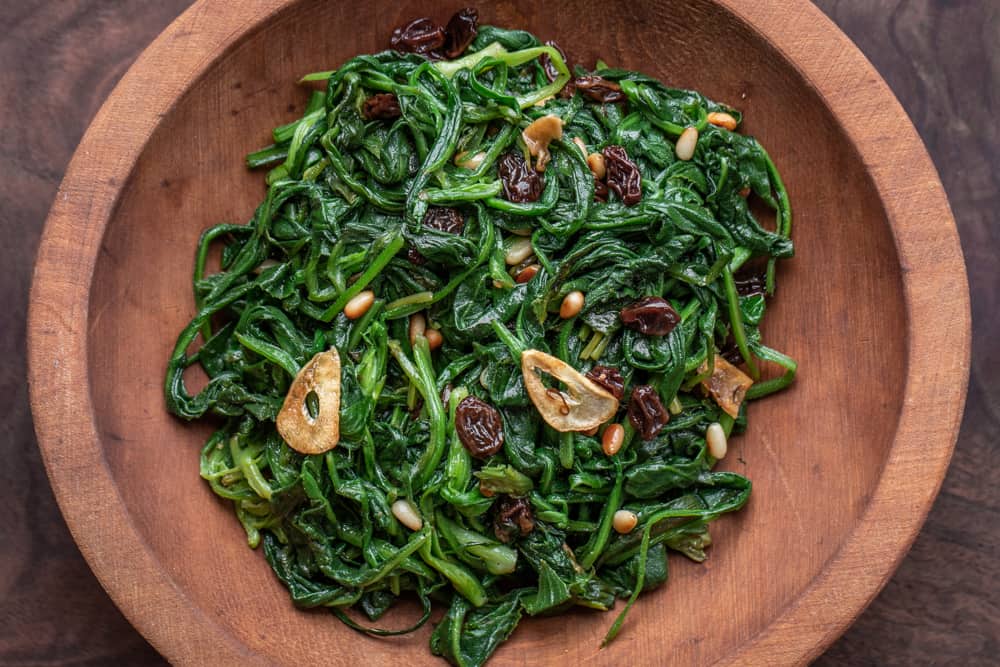 a bowl of cooked greens with garlic, raisins and pine nuts 