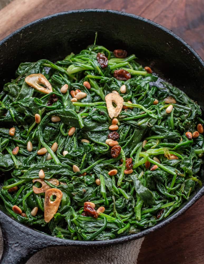 a pan of cooked greens with raisins and pine nuts 